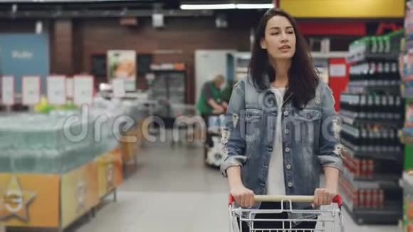 漂亮的小姐走在超市的过道上购物车里放着商品的货架视频的预览图