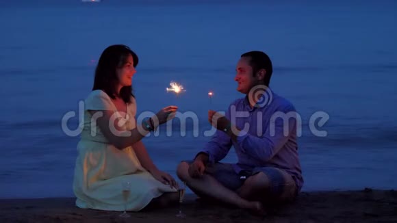 浪漫情侣在日落时分在海滩上用烟花和香槟庆祝视频的预览图