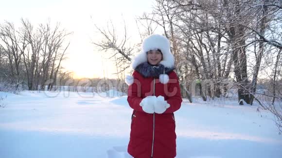 幸福的女孩在森林里日落时双手举起雪雪在阳光下落下闪闪发光冬天孩子们玩视频的预览图