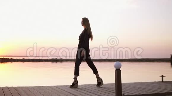 慢动作从木墩旁走着的美丽的长发黑衣女子的侧面拍摄的清晨黄昏视频的预览图