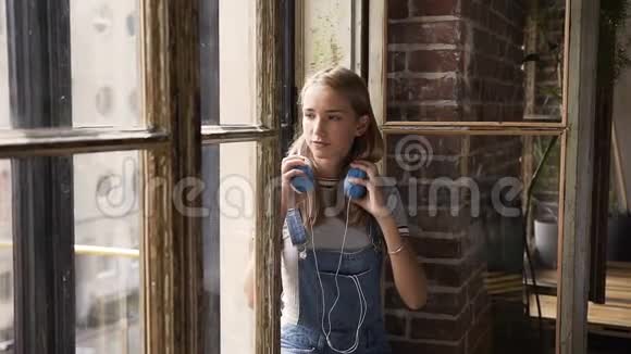 窗户背景上年轻迷人的女孩用耳机听音乐的肖像休闲和放松视频的预览图