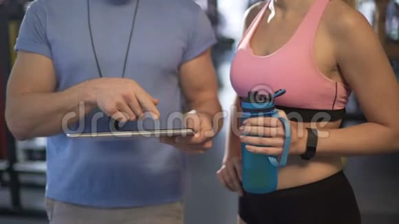 教练向女性客户解释培训时间表在健身房使用平板电脑视频的预览图