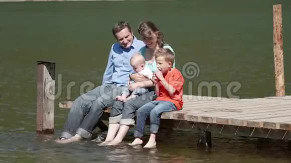 年轻的父母带着两个孩子在浮桥上一家人赤脚欣赏大自然弟弟带着父母度假视频的预览图