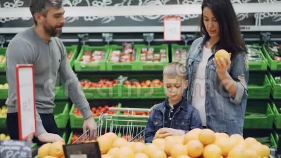 快乐的一家人在超市里挑选橘子爸爸妈妈和可爱的男孩正在吃水果闻闻它们然后把它们放进去视频的预览图