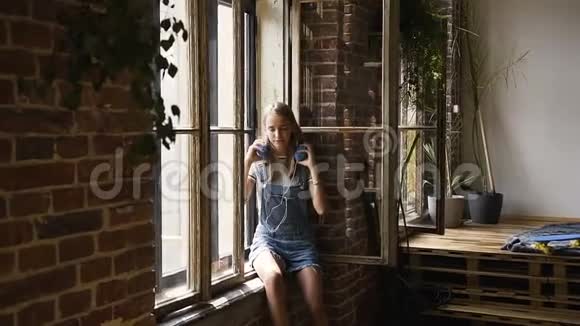 留着长发的漂亮少女听耳机里的音乐女孩坐在窗边听蓝色的音乐视频的预览图