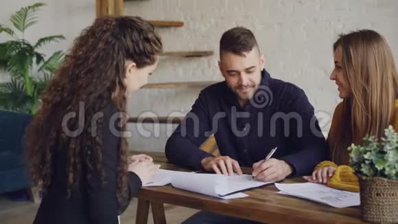 年轻人笑着签订买卖合同然后在与房地产经纪人见面时拿钥匙拥抱视频的预览图