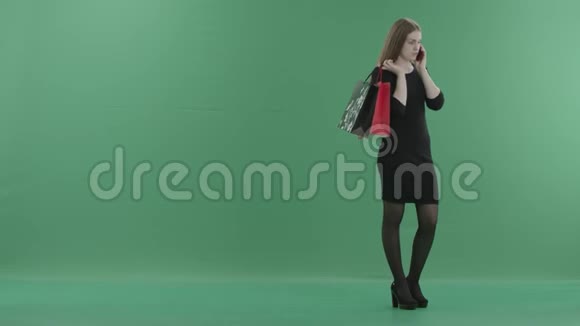 穿着小黑裙子的漂亮女人拿着购物袋在手机上说话她站在视频的预览图