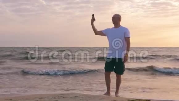 日落时分帅哥在海边的海滩上打电话自拍视频的预览图