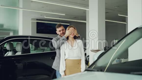 迷人的年轻女子正在从她的男朋友那里买新车他闭上眼睛带她开车视频的预览图