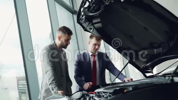 有经验的汽车经销商正在打开引擎盖展示新的客户引擎并告诉他质量和特点视频的预览图