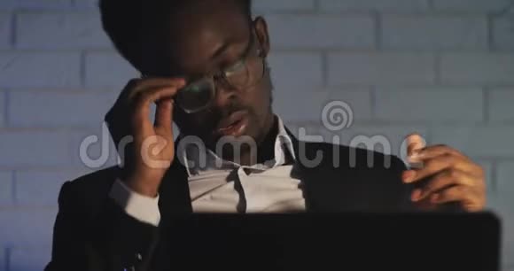 厌倦了在电脑上工作年轻的黑人男子举起眼镜擦眼睛工作狂努力工作视频的预览图