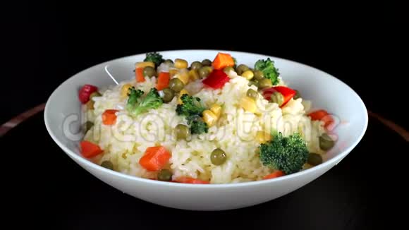 在白色盘子里放着蔬菜青菜和红椒的米饭在黑色背景上旋转视频的预览图