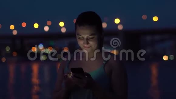 女孩在夜间海滩散步时使用智能手机高清高清视频的预览图