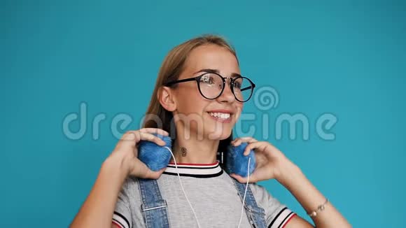 戴着耳机听音乐和跳舞的戴着眼镜留着长发的少女的肖像视频的预览图