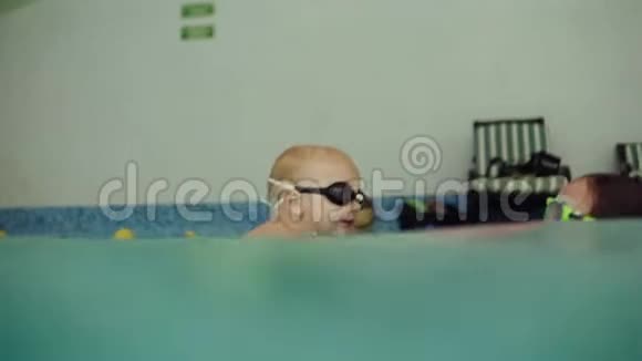 侧面观看水下拍摄的年轻女子穿着粉红色泳衣在游泳池里支撑着他的儿子如何教学视频的预览图