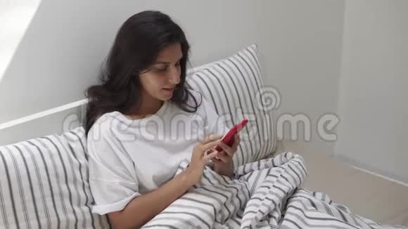 学生女孩早上坐在床上用手机发信息视频的预览图
