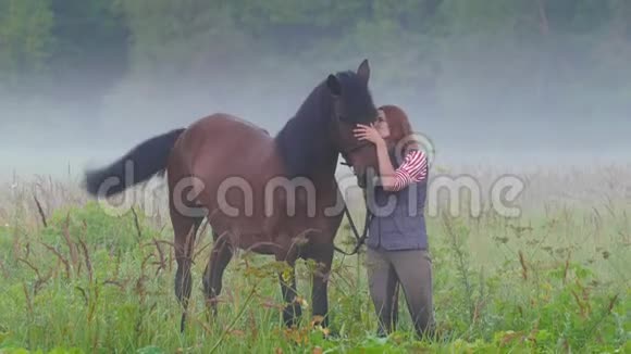 一个年轻的女人站在一匹马旁边在雾中抚摸着他的头视频的预览图