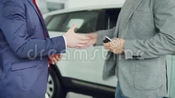 汽车陈列室的男工正在给买车的年轻人送车钥匙并和他站在豪华的旁边握手视频的预览图