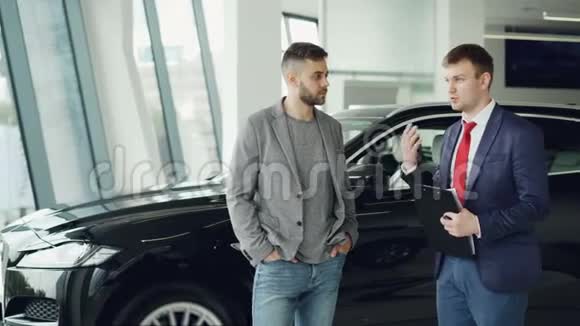 帅哥在车展上和汽车经销商经理谈论新的汽车型号经销商正在持有视频的预览图