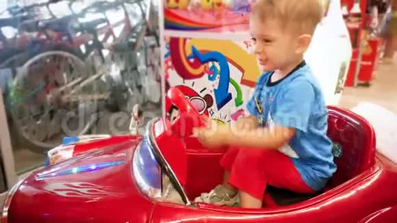 4k视频快乐微笑幼儿男孩骑在硬币操作玩具车在商场视频的预览图
