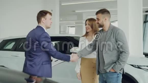 一位成功的年轻人正在为他的妻子买车与经销商握手然后亲吻迷人的女人视频的预览图