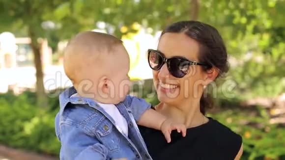 一位戴太阳镜的年轻母亲和她刚出生的儿子在阳光公园散步视频的预览图