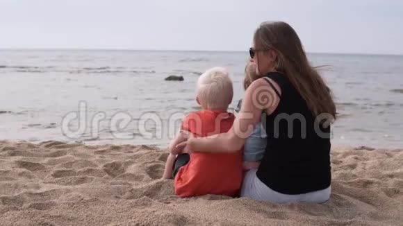 妈妈和孩子们坐在海边的海滩上视频的预览图