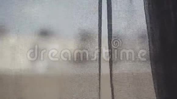 清晨窗上透明的灰色窗帘被风轻轻地抚摸着从窗户看到的城市景色视频的预览图