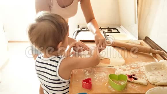 年轻母亲教她的小儿子用特殊的塑料刀切面团做饼干视频的预览图