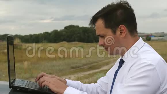 穿着蓝白衬衫的男商人正在汽车车顶上的电脑上工作视频的预览图