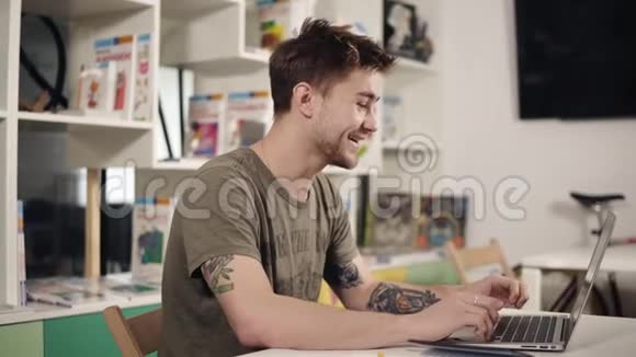 20岁的迷人男程序员在笔记本电脑键盘上打字时笑了视频的预览图