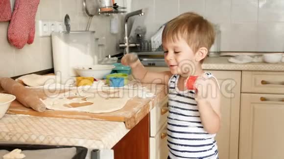 4k镜头快乐微笑的幼儿男孩一边在厨房里玩面团一边做饼干视频的预览图