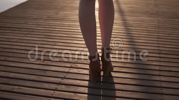 早晨的日出一个穿着高跟鞋和长袍的苗条女孩走在木码头的背面镜头海滨视频的预览图