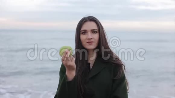 一个穿着绿色外套吃苹果的漂亮女孩的特写背景中的海洋视频的预览图
