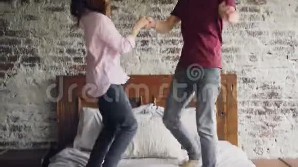 快乐的恋人们手牵着手在床上跳舞一起享受婚姻生活现代双人床砖墙和视频的预览图