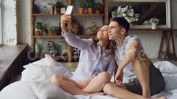 一对快乐的情侣正在用智能手机自拍看相机摆姿势坐着做滑稽的表情视频的预览图