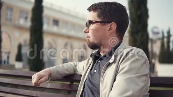 大胡子坐在户外的长凳上享受着春天城市的新鲜空气视频的预览图