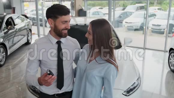 参观汽车经销商漂亮的夫妇拿着他们新车的钥匙看着相机微笑着视频的预览图
