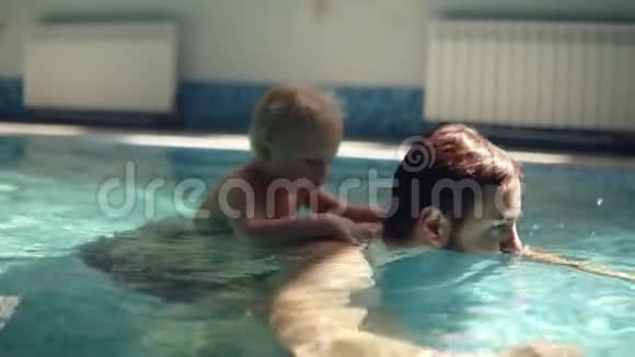 年轻人背着金发的儿子在水下划船小男孩在水面上印度游泳池视频的预览图
