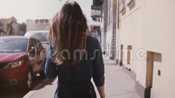 镜头跟随年轻的学生女孩穿着一件蓝色的连衣裙长发随风在街上缓慢地走着视频的预览图