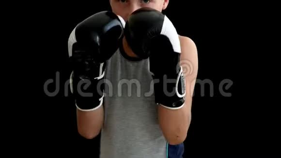 一个青少年站在黑暗的背景上戴着拳击手套那男孩有黑白手套几乎遮住了他的脸视频的预览图