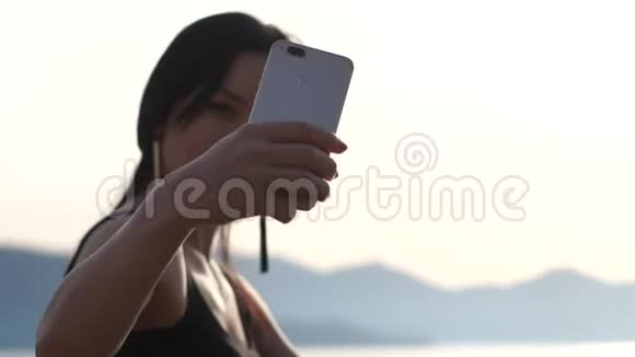 一个年轻的女孩在大海的背景上慢镜头拍摄自拍照片视频的预览图