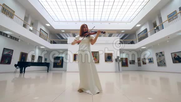 穿着白色连衣裙的音乐家正在艺术大厅里拉小提琴视频的预览图