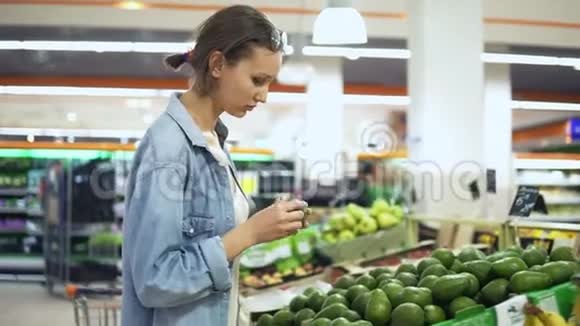 杂货店的蔬菜水果部美女在随意挑选绿色鳄梨手持录像视频的预览图