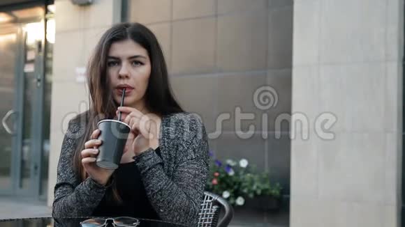 年轻女子坐在户外的桌子旁喝咖啡视频的预览图