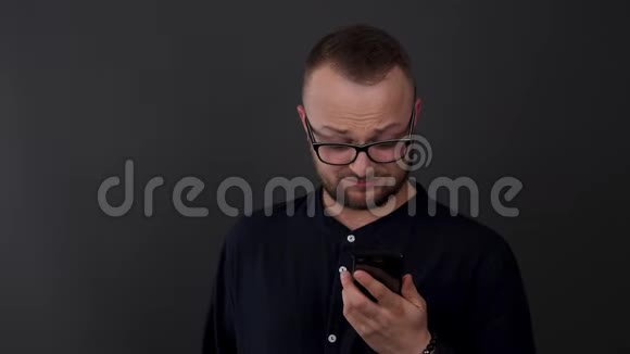 一个戴眼镜的留胡子的年轻人工作室拍摄的男性轻蔑反应他看到的电话视频的预览图
