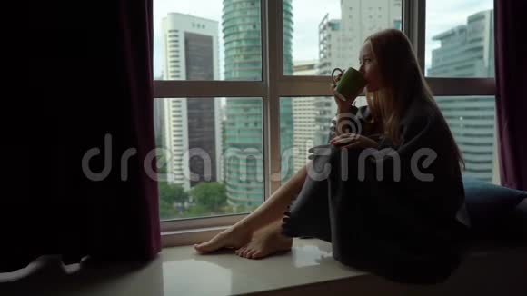 超级慢动作镜头一个年轻的女人喝茶或咖啡包裹在格子坐在全景窗口视频的预览图