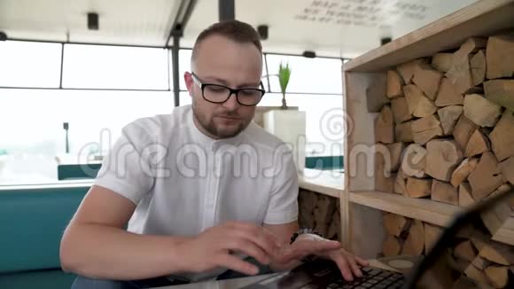 一个戴眼镜的留着胡子的年轻人在露台上的笔记本上工作接到一个电话视频的预览图