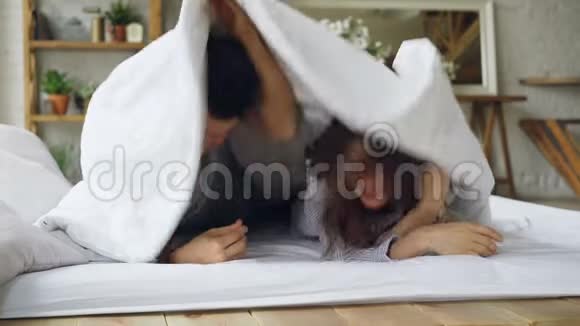 一对幸福的夫妇躺在毯子下的床上然后露出脸来看着镜头笑着爱视频的预览图