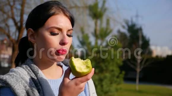动作缓慢特写迷人的年轻黑发女人美丽的眼睛和红唇吃绿苹果视频的预览图